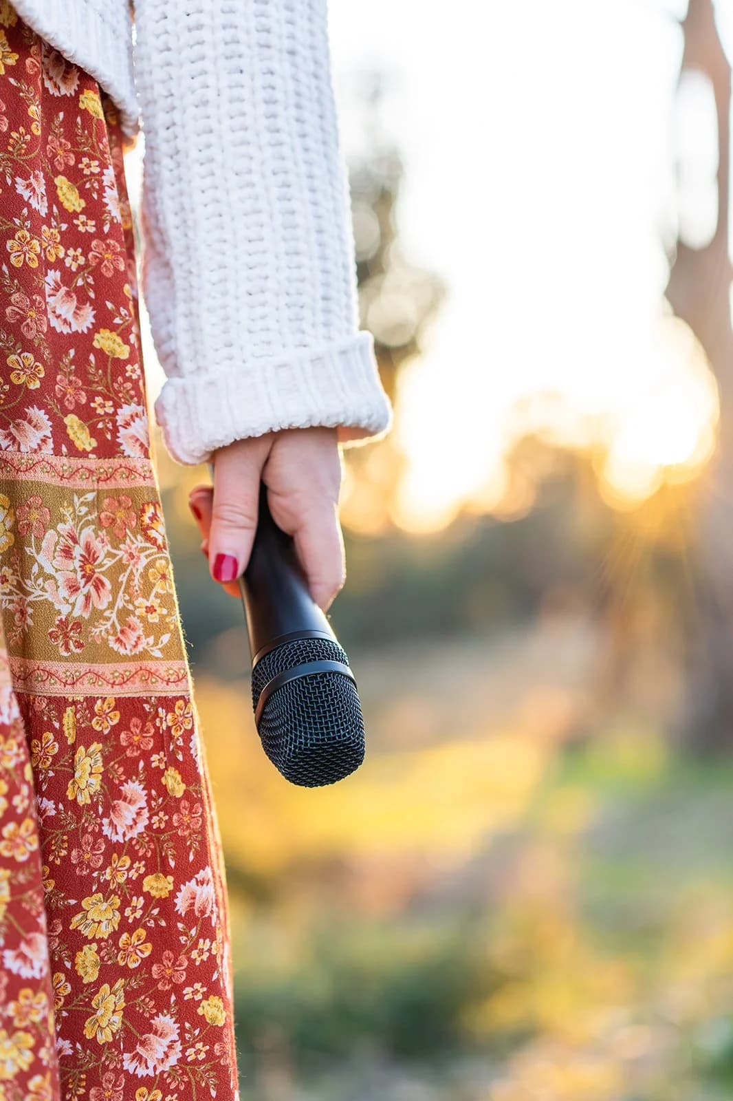 Tam holding a microphone in soft evening light.